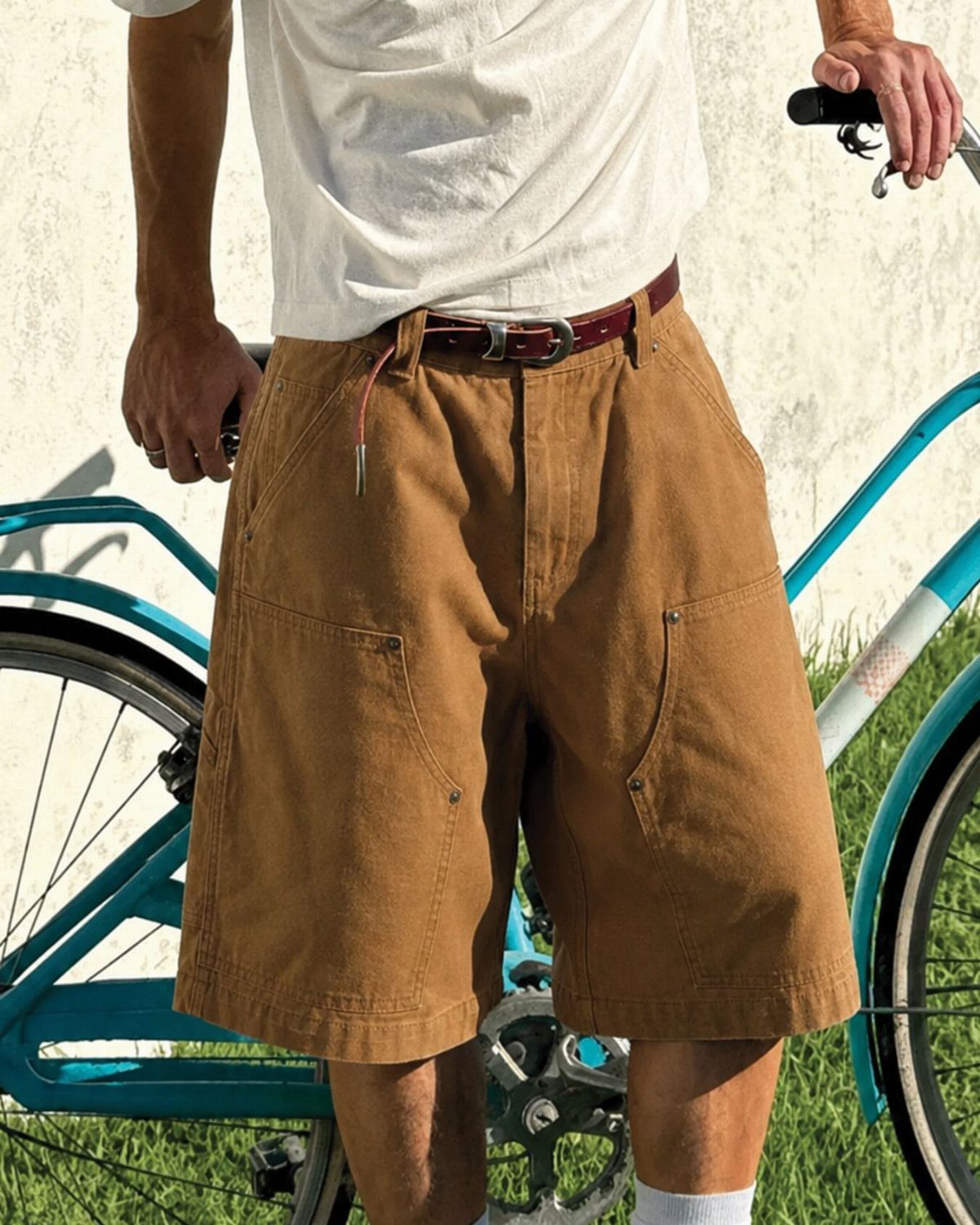 Brown canvas shorts worn by a person standing next to a blue bicycle.