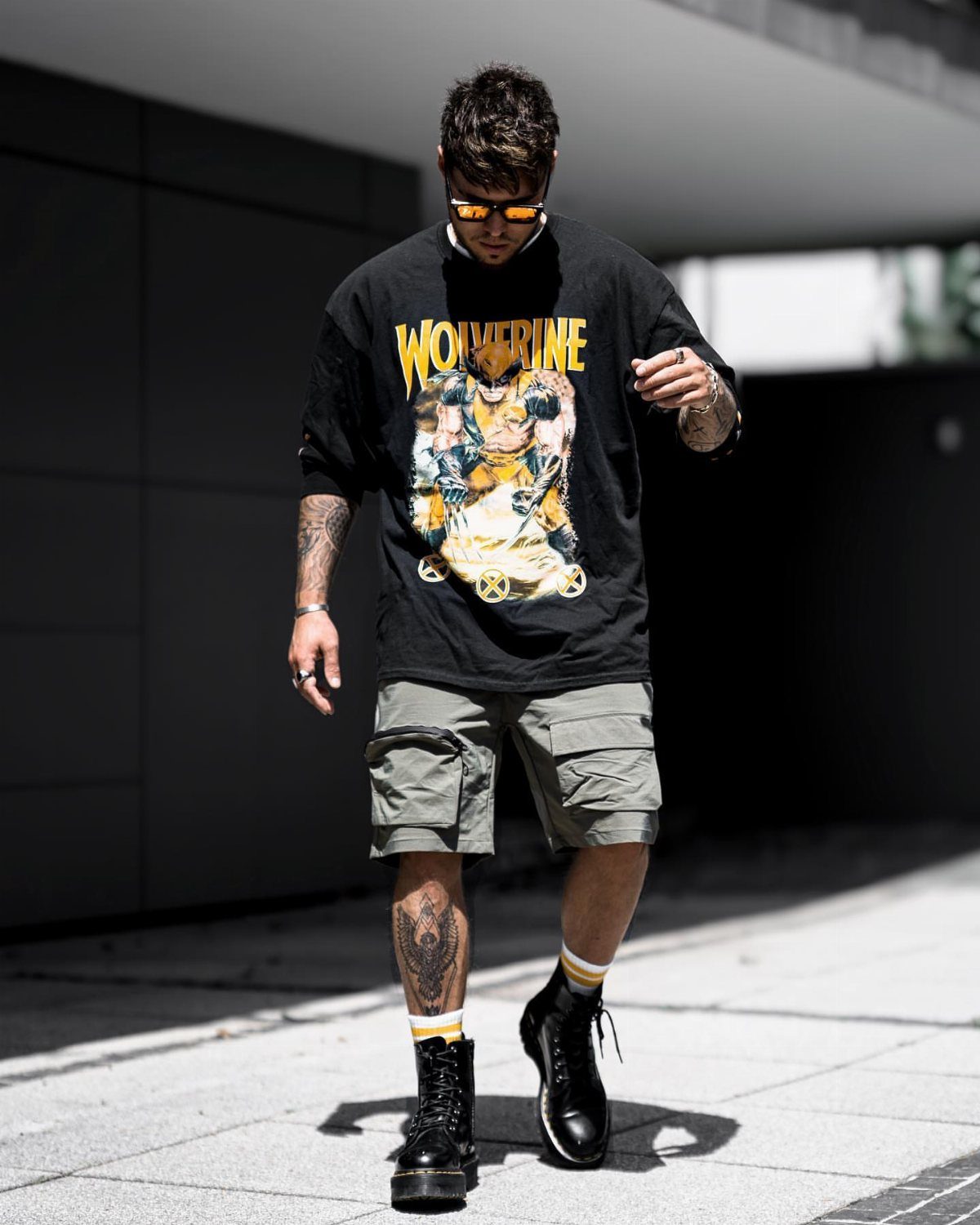 Man wearing a black graphic t-shirt and grey cargo shorts with black boots.