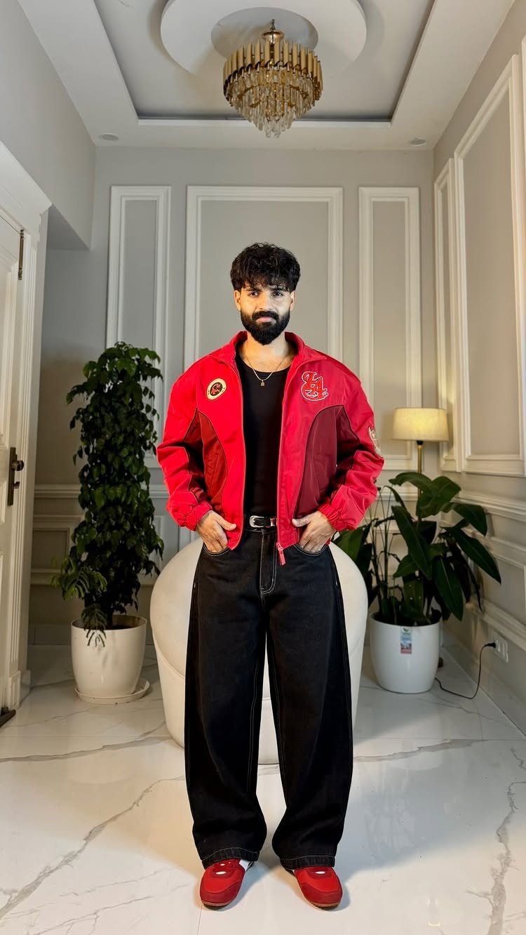 Man wearing a red oversized bomber jacket and wide-leg black trousers in a room.