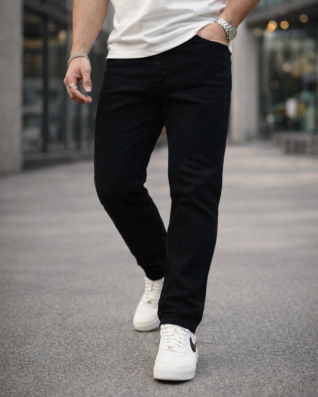 Man wearing black straight leg jeans, white t-shirt, and white sneakers outdoors.