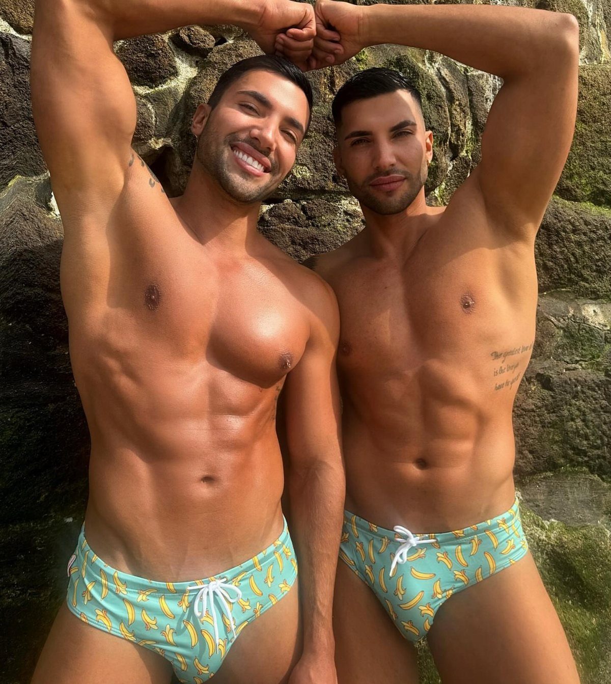 Two muscular men wearing light blue swim briefs with yellow banana patterns.