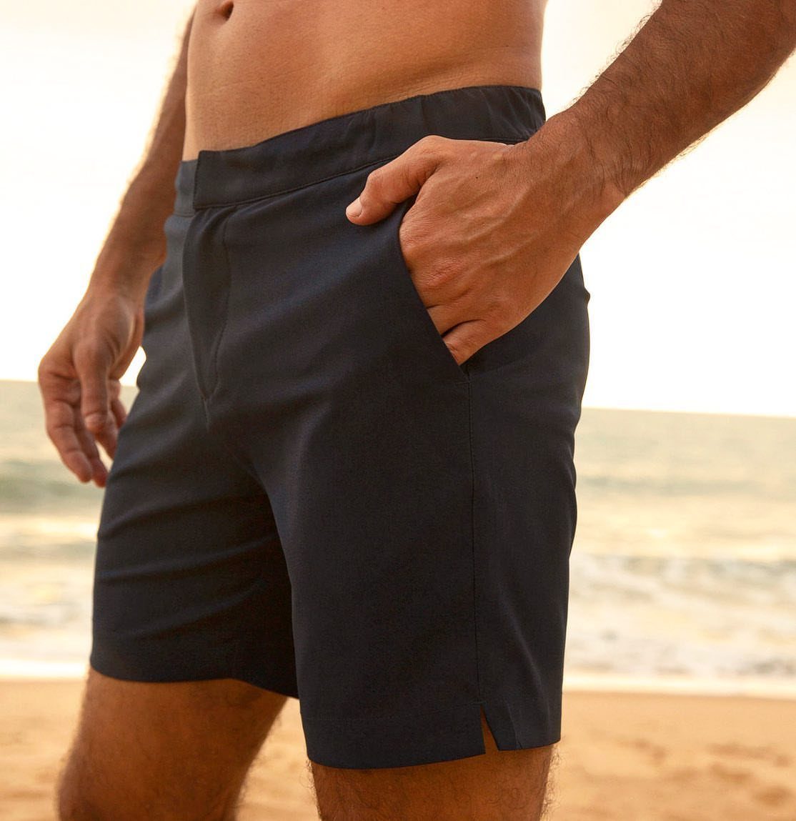 Man wearing dark navy blue tailored swim shorts on a sandy beach.