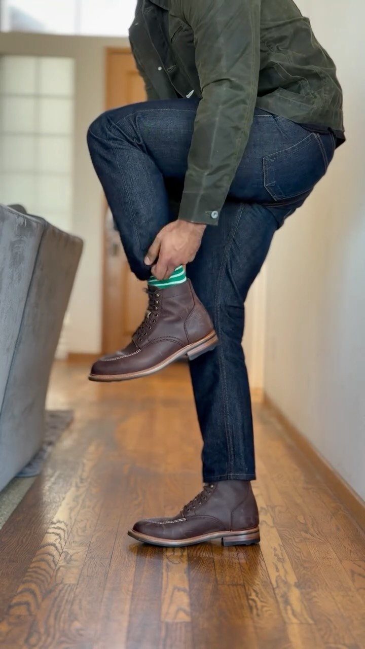 Brown leather chukka boots worn with dark blue jeans and a green jacket.