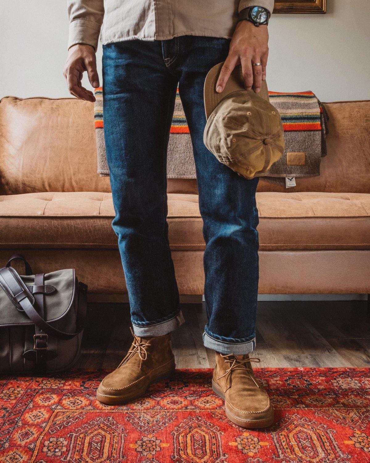 Tan suede chukka boots worn with cuffed dark blue jeans on a rug.