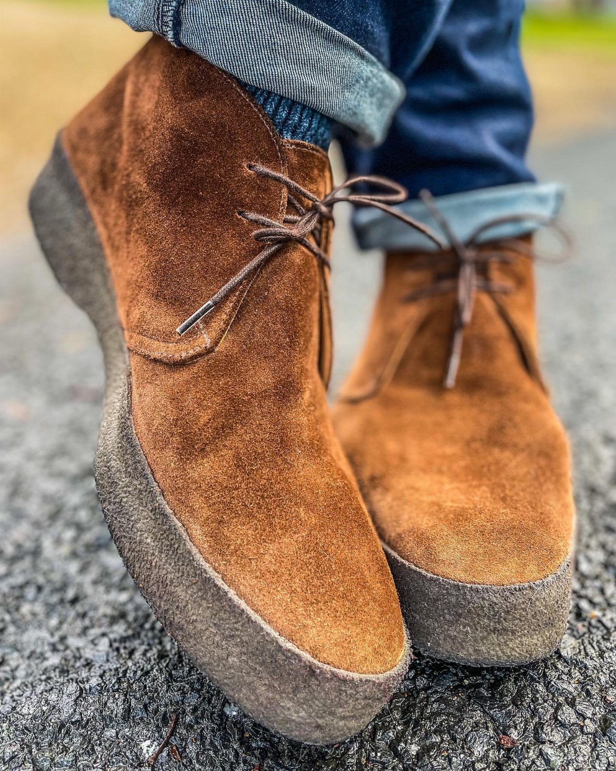 Brown suede chukka boots with thick soles and cuffed blue denim jeans.