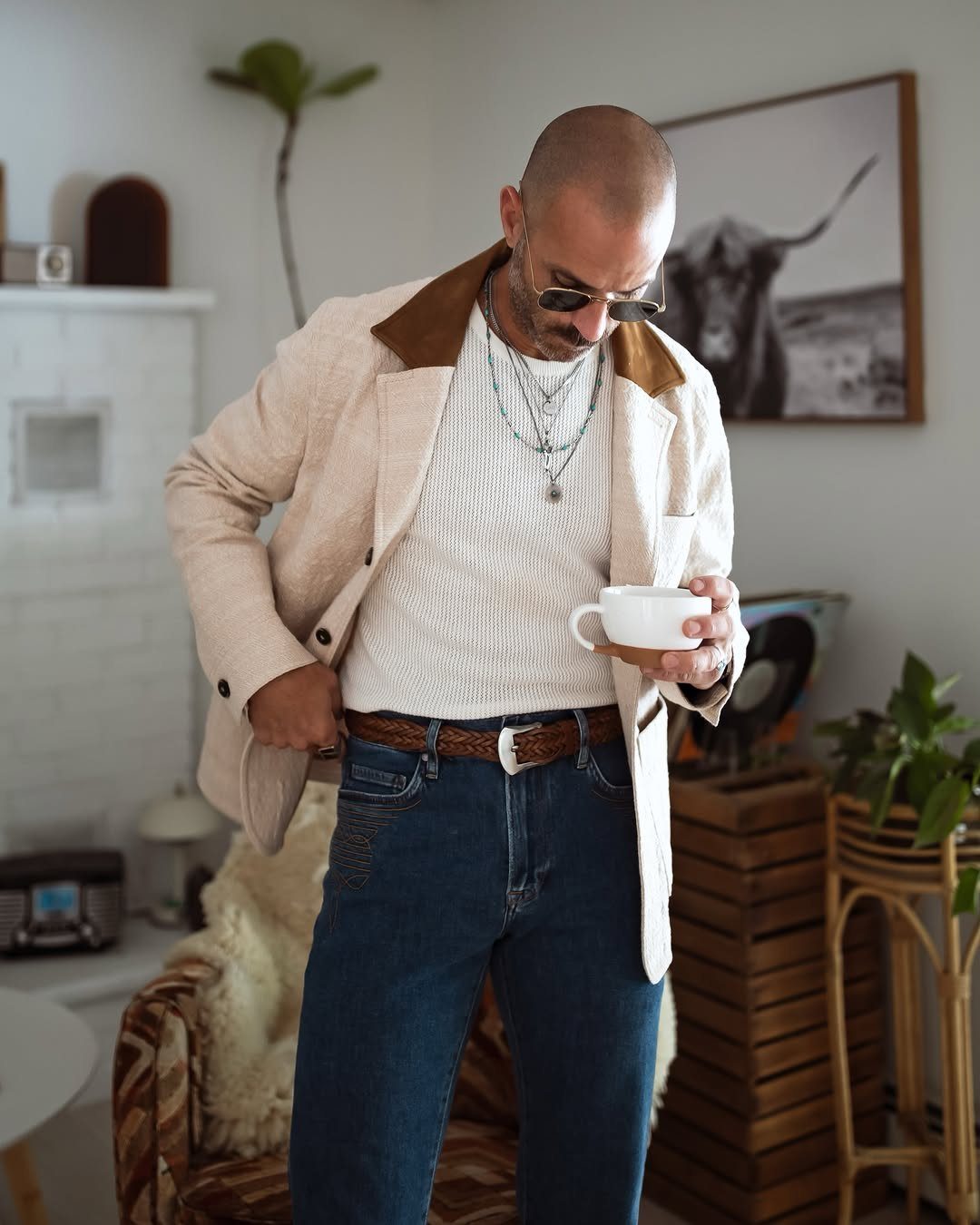 Man wearing a beige blazer with brown collar and white sweater holding coffee cup.