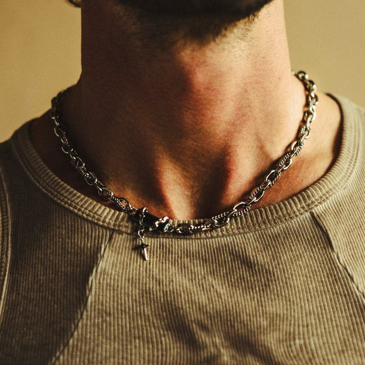 Silver chain necklace with a cross pendant worn over a beige ribbed shirt.