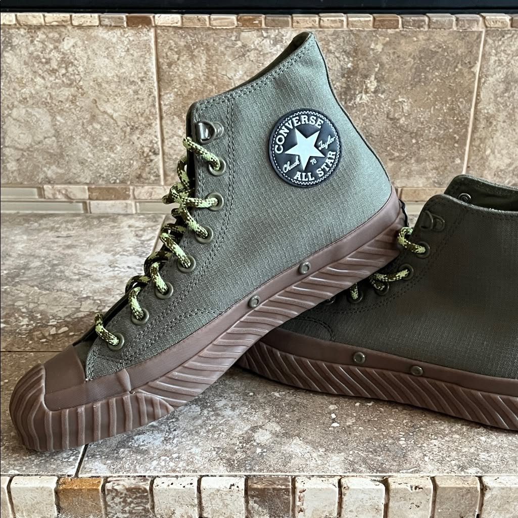 Olive green canvas high-top Converse sneakers with yellow-green laces on stone tiles.