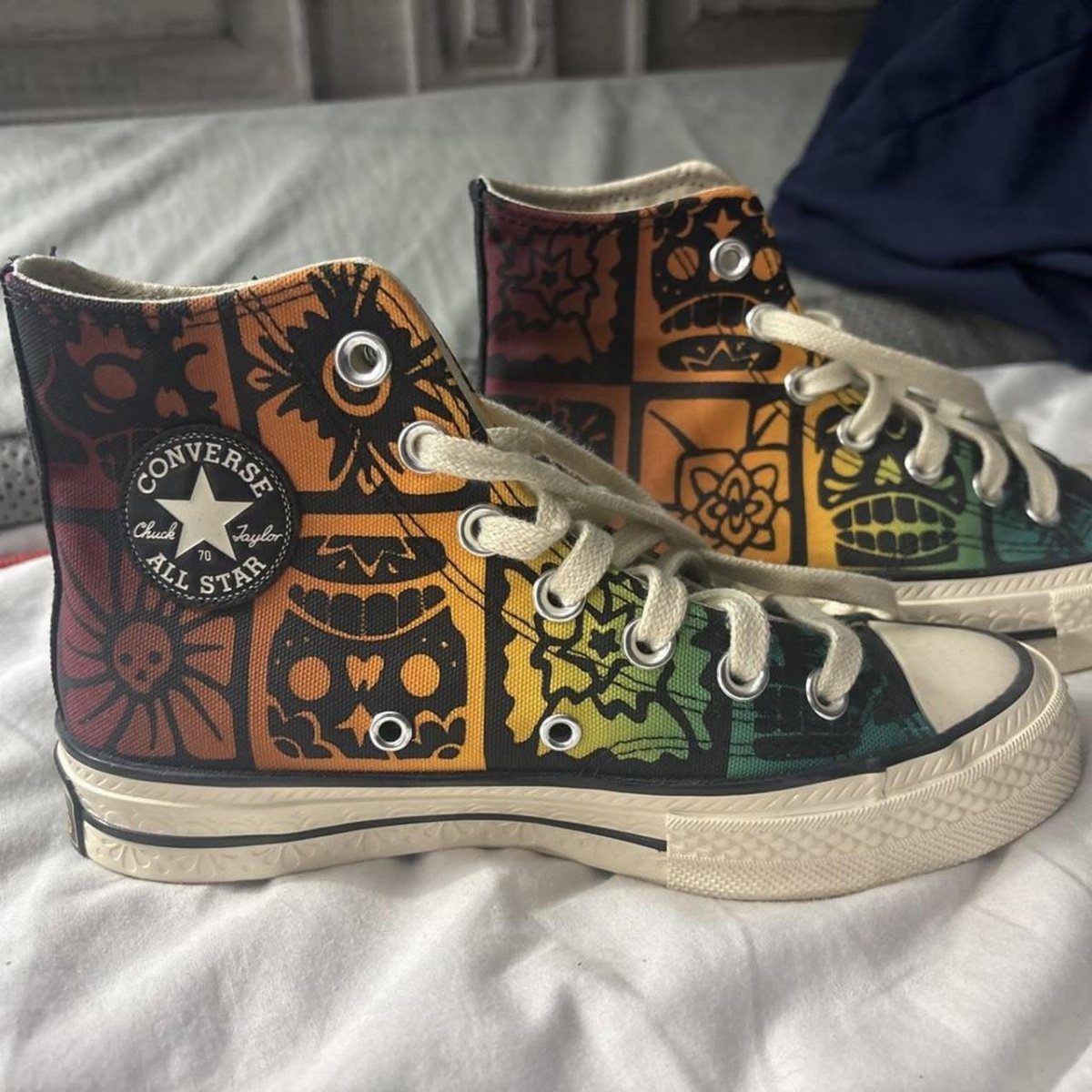 High-top Converse sneakers with colorful sugar skull patterns on a white fabric background.