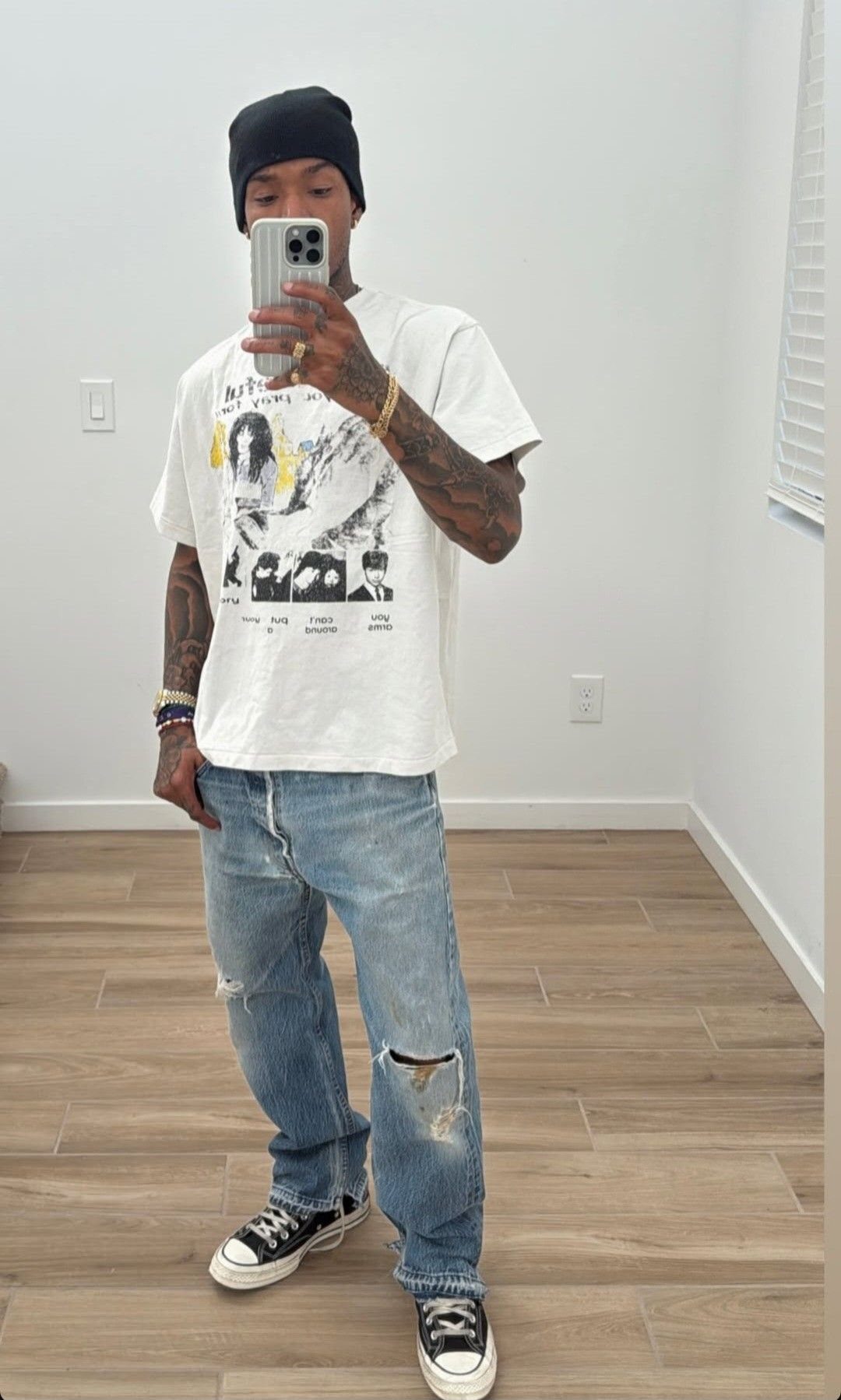 Man wearing black Converse sneakers and ripped blue jeans taking a mirror selfie.