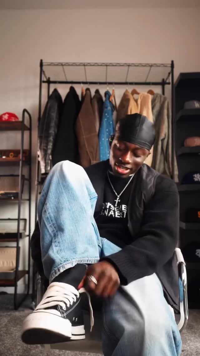 Man wearing black high-top Converse sneakers and light blue jeans in a room.