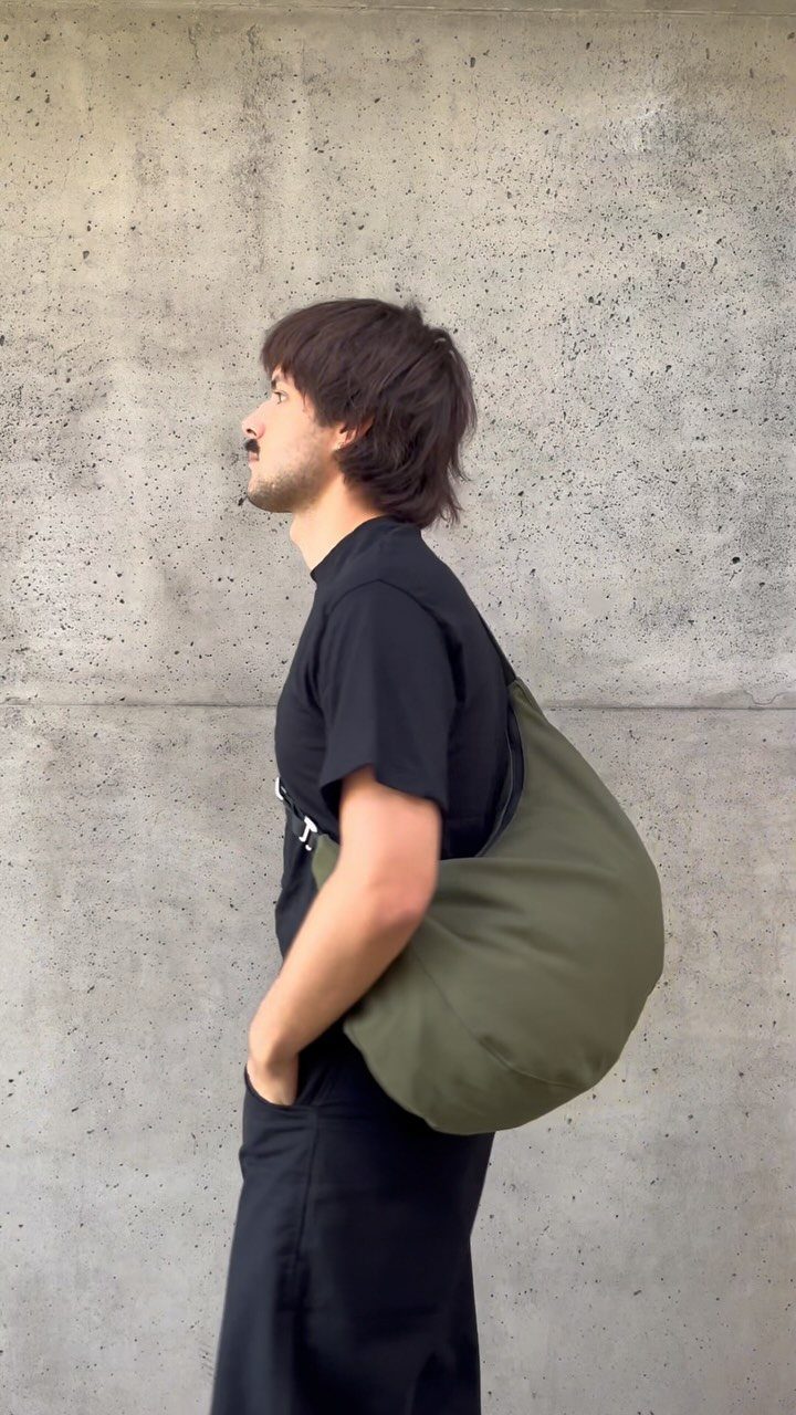 Men's Fashion Crossbody Bag: 6 Styles Worth Carrying 2 Man wearing an olive green nylon crescent crossbody bag against a concrete wall