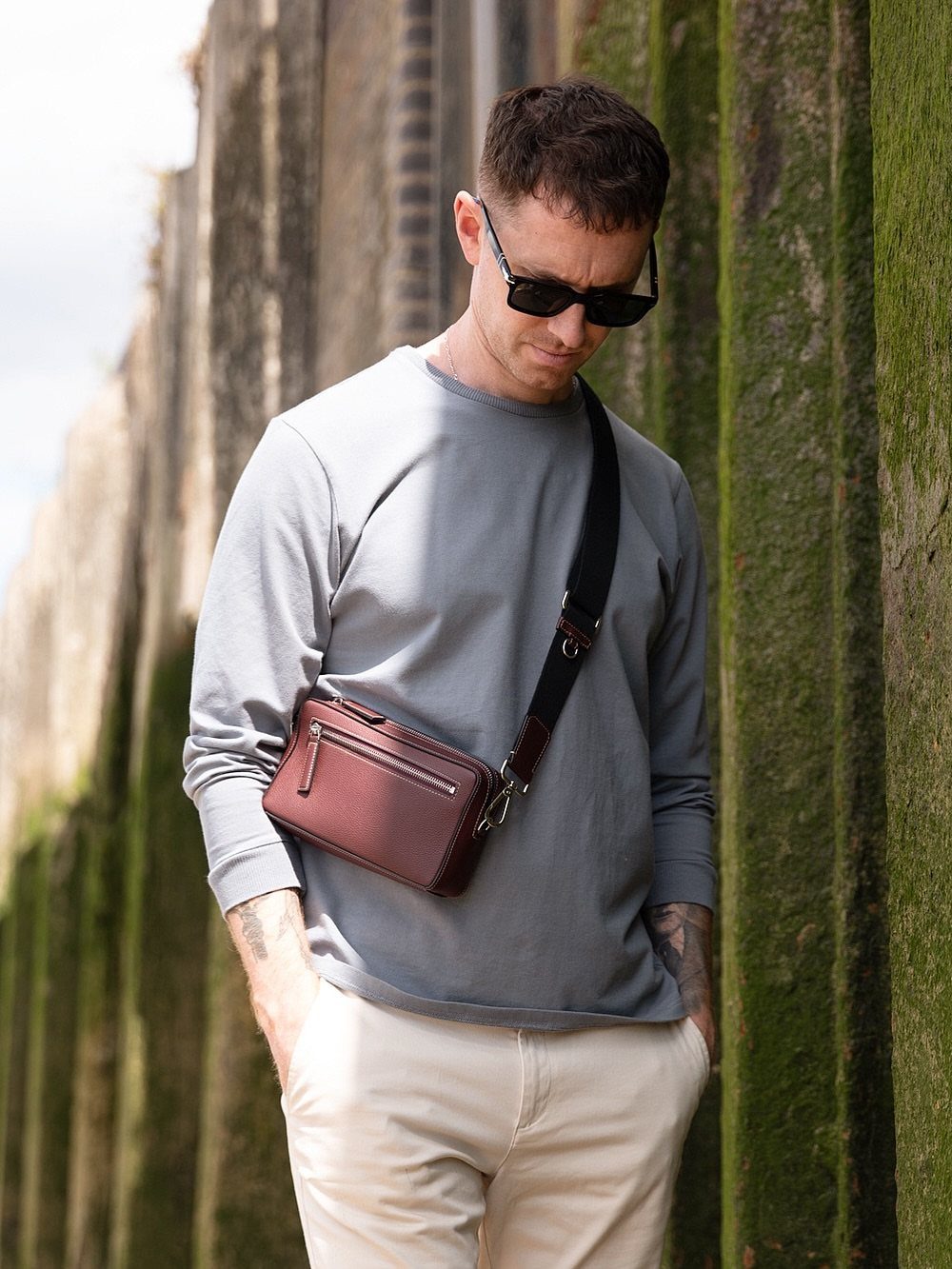 Men's Fashion Crossbody Bag: 6 Styles Worth Carrying 6 Man wearing a burgundy leather crossbody bag with a grey shirt and white trousers.