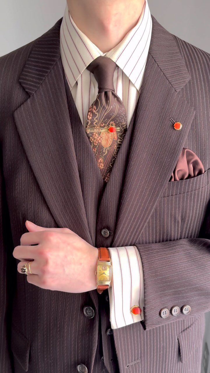 Man in a brown pinstripe three-piece suit with a patterned tie and gold accessories.