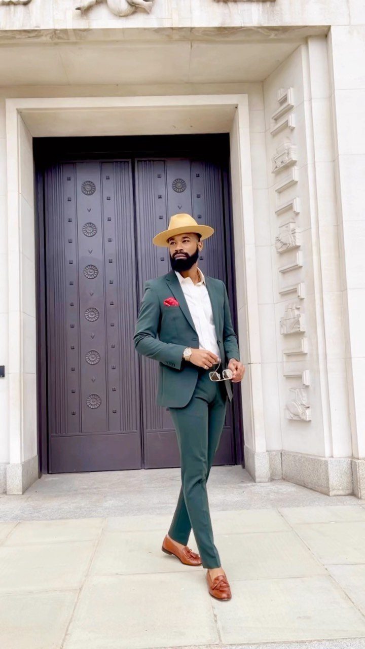 Man in a green suit and tan hat posing before ornate brown doors.