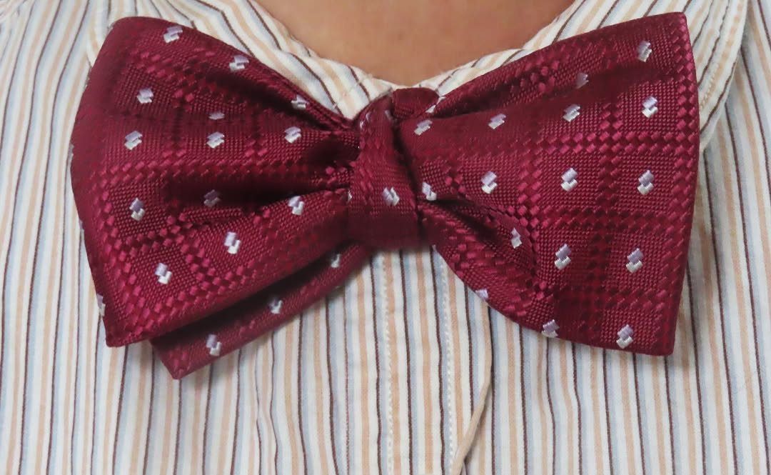 Burgundy bow tie with white patterns on a striped dress shirt.