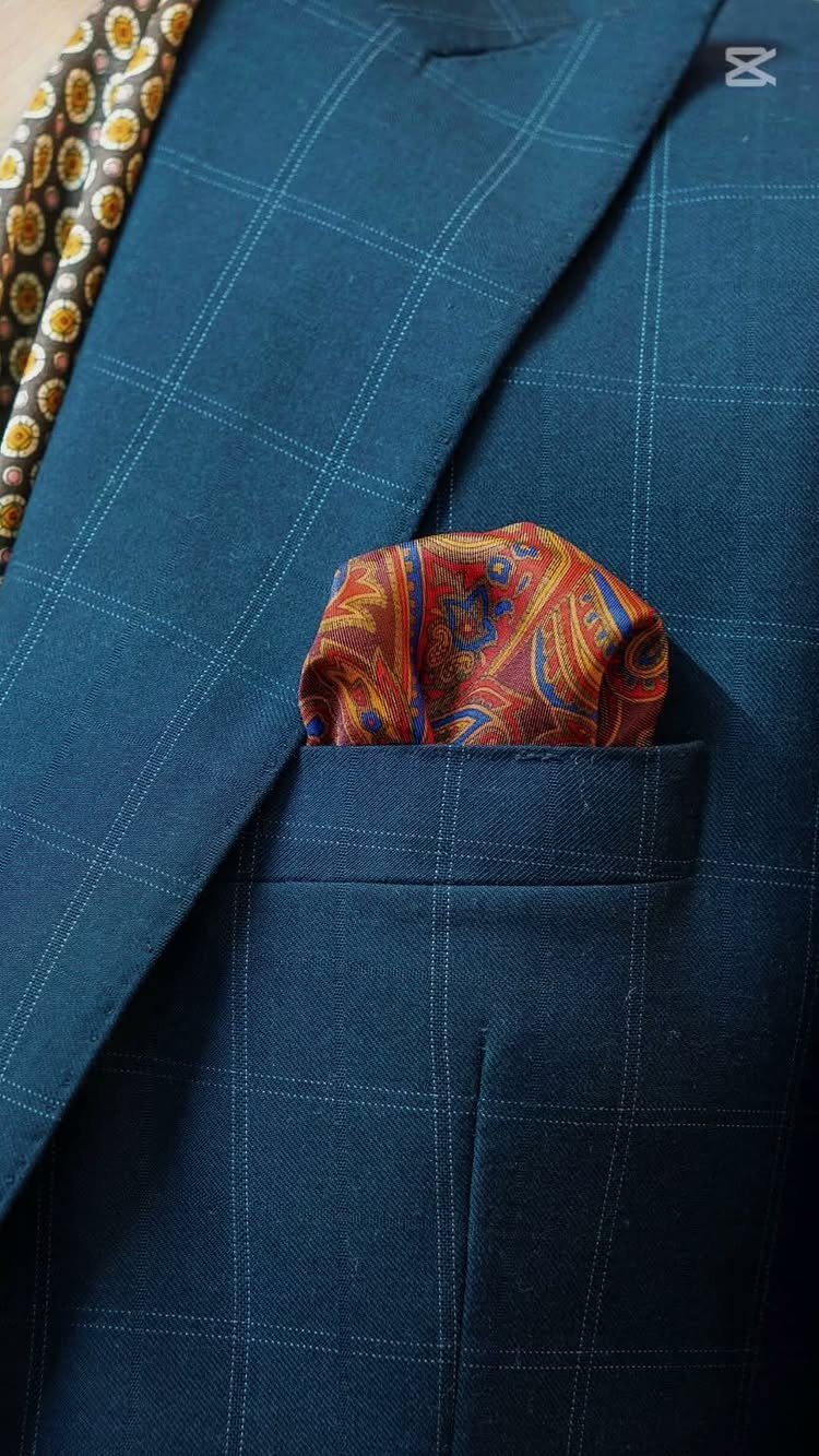 Red paisley pocket square in the breast pocket of a teal windowpane suit.