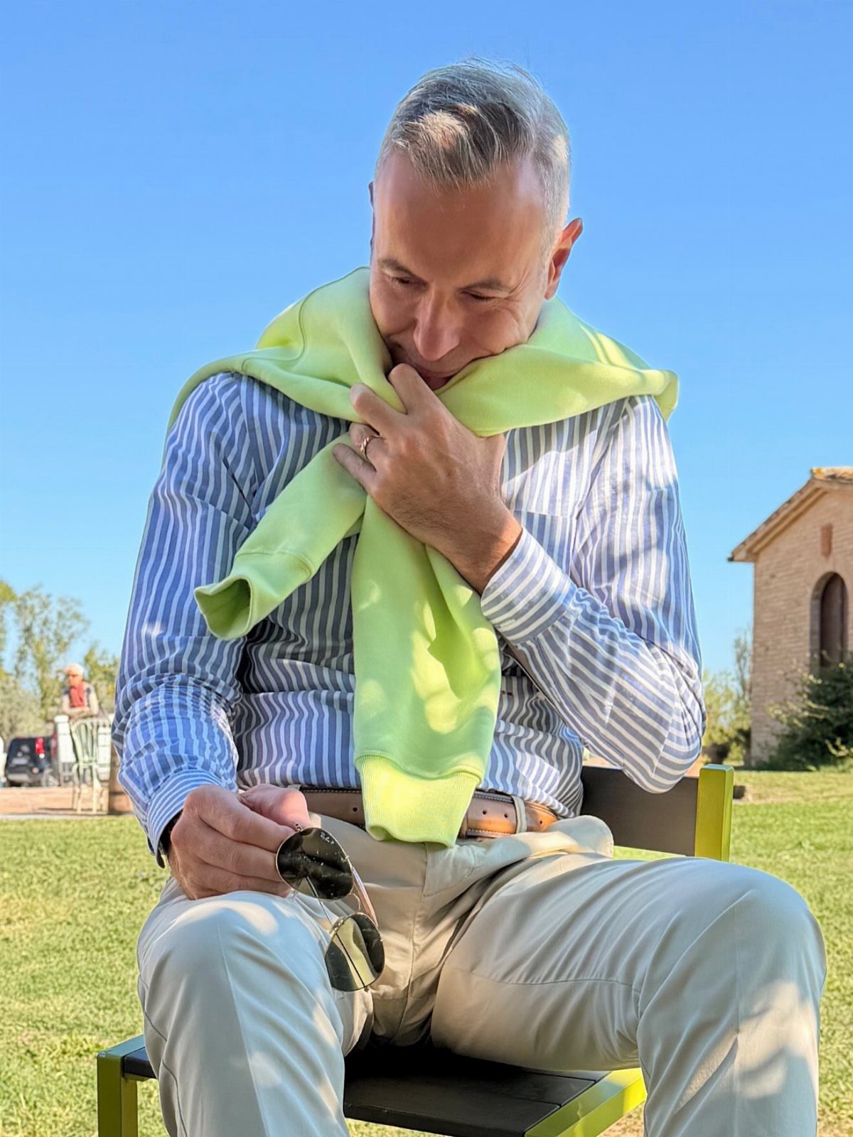 Man in striped shirt and beige pants with lime green sweater over shoulders.