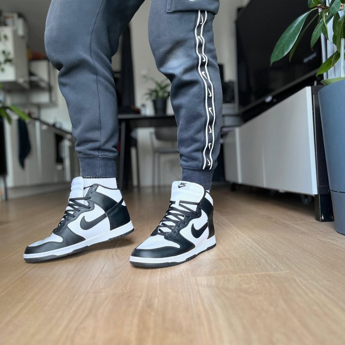 Black and white leather Nike Dunk high-top sneakers worn with grey joggers.