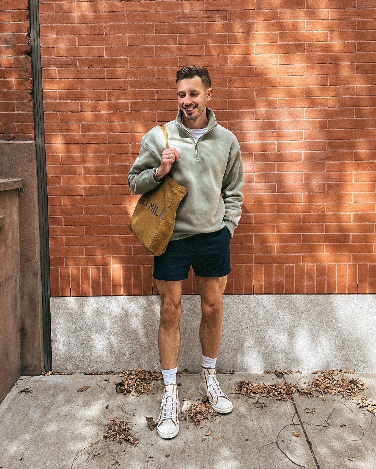 Man in grey pullover and navy shorts wearing white high top sneakers