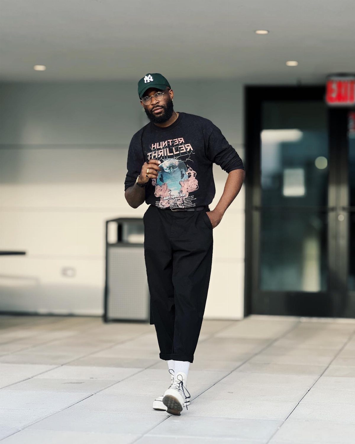 Man in black outfit and green cap wearing white high-top sneakers.