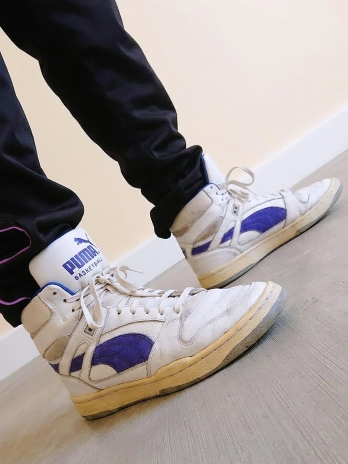 White and purple high-top Puma basketball sneakers worn with white socks and black pants.