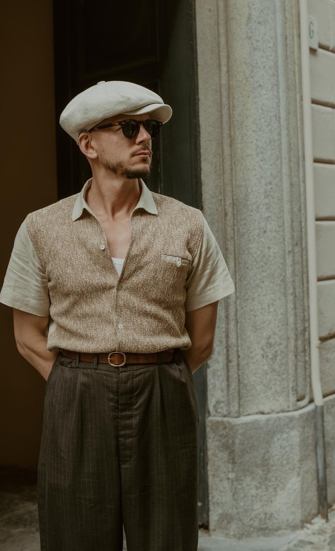 Man in vintage 1960s style clothing including a flat cap and high-waisted trousers.