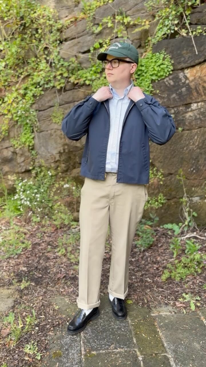 Person wearing a dark blue Harrington jacket and khaki pants against a stone wall.