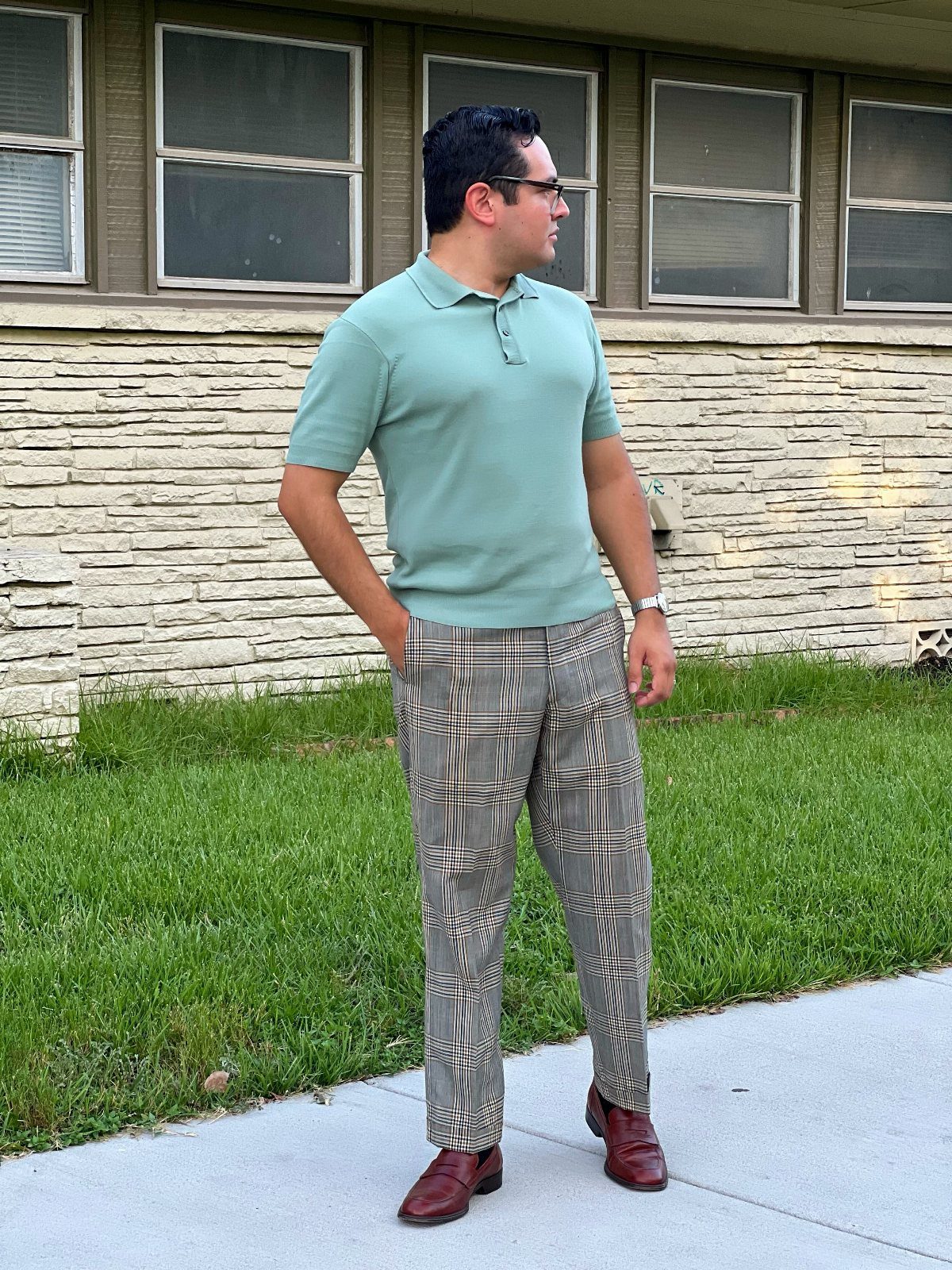 Man wearing a light green polo shirt and plaid slim-fit trousers standing outdoors.