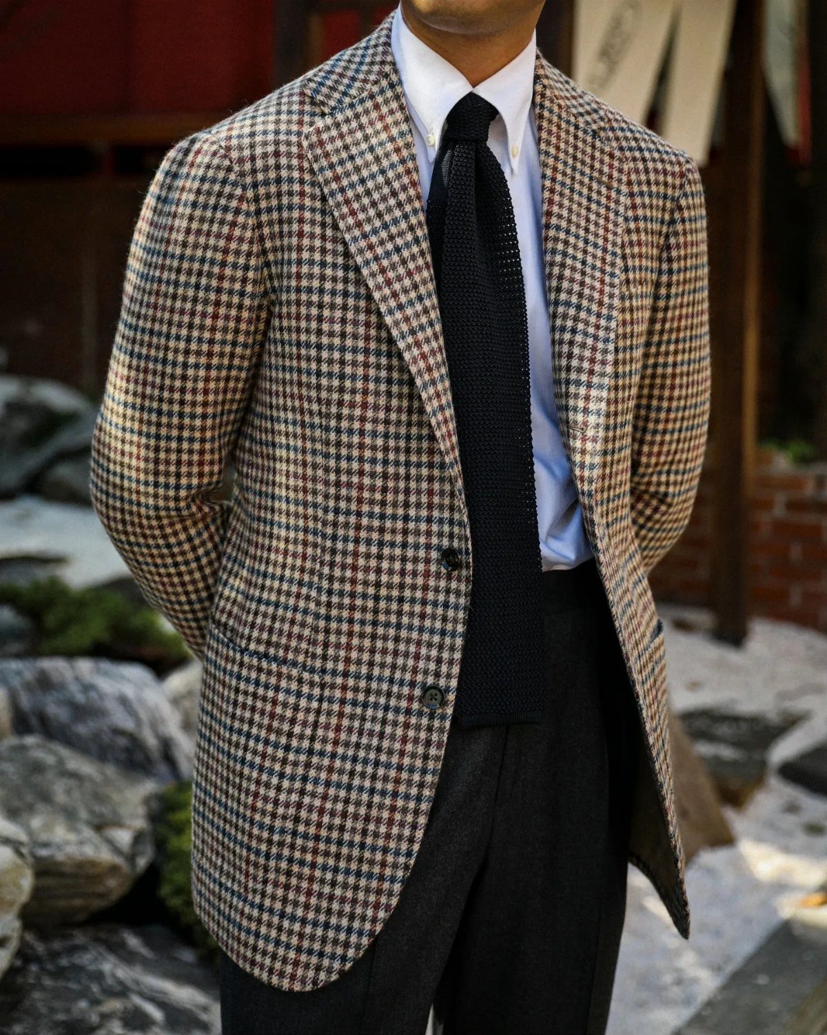 Man wearing a brown houndstooth sport coat, white shirt, and black knitted tie.