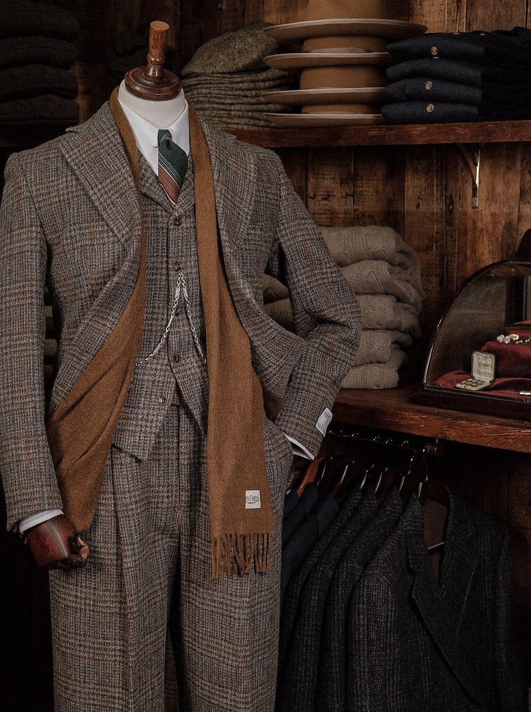 Three-piece tweed suit with a brown scarf on a mannequin in a tailor shop.