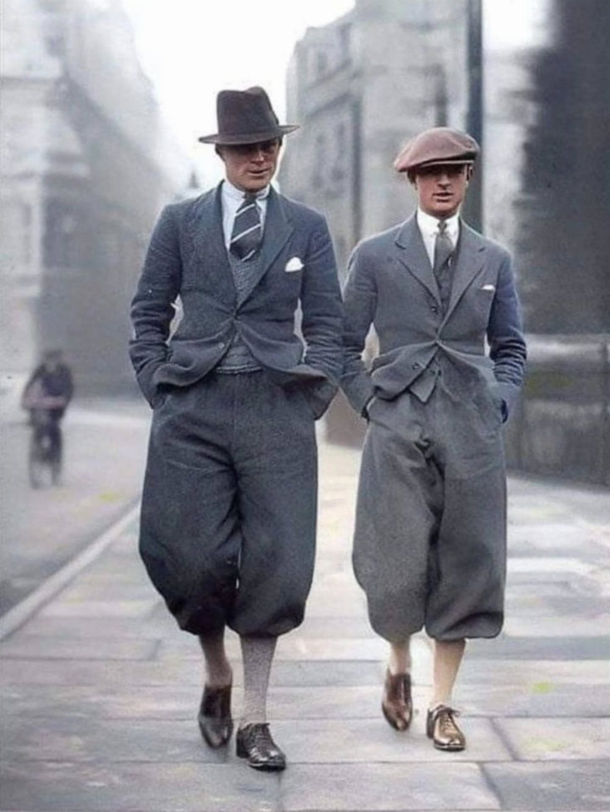 Two men in 1920s suits and knickerbockers walking on a city sidewalk.