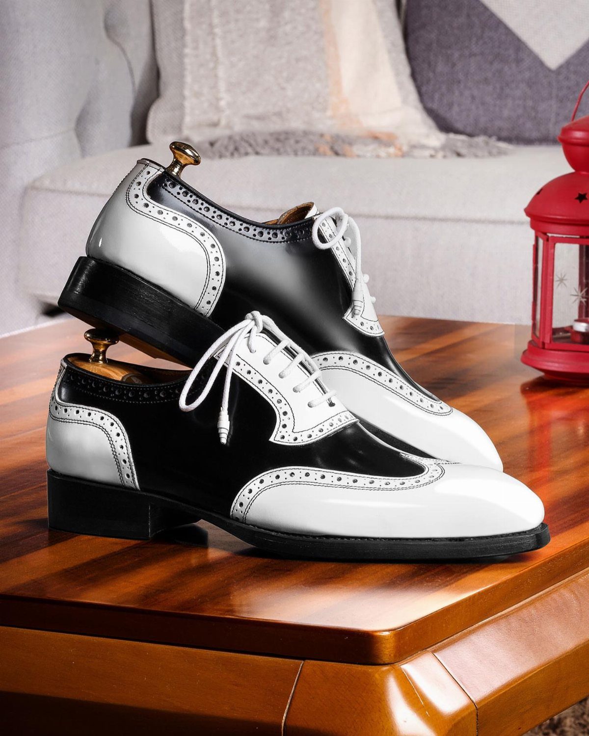 Black and white wingtip oxford shoes on a polished wooden table.