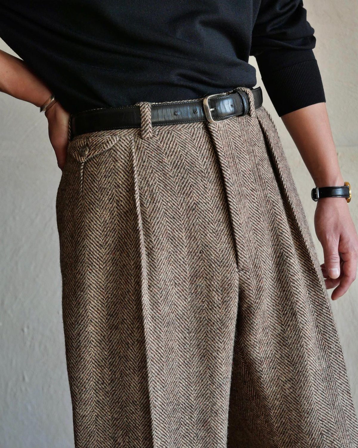 High-waisted brown herringbone tweed trousers with a black belt and black top.