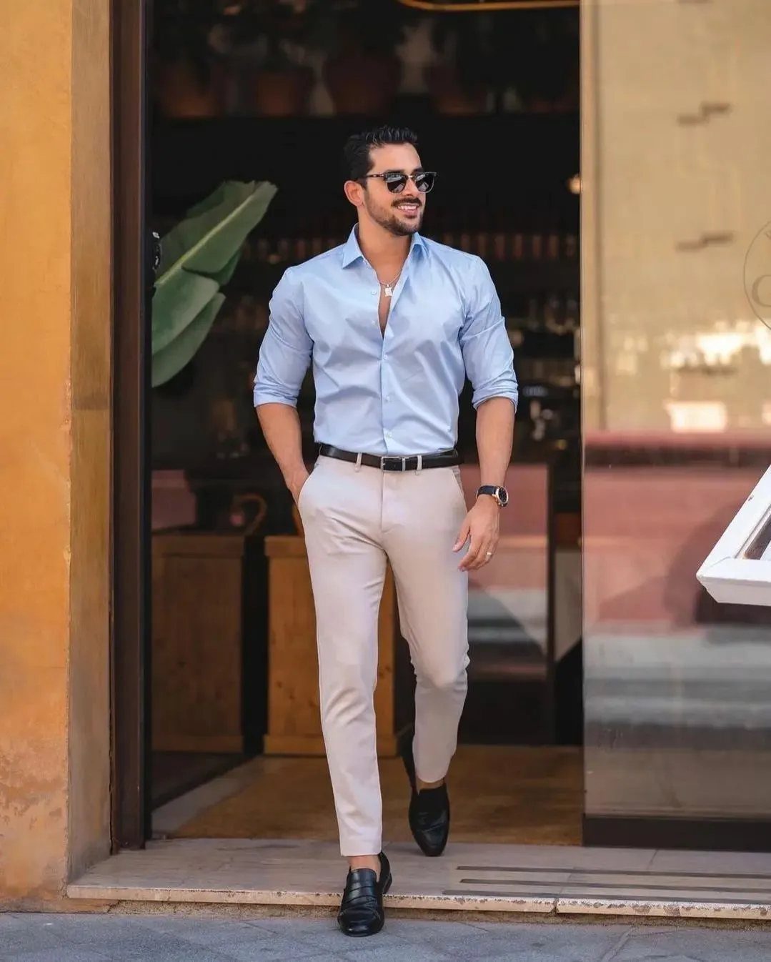 Man in light blue shirt and beige trousers walking through a doorway.