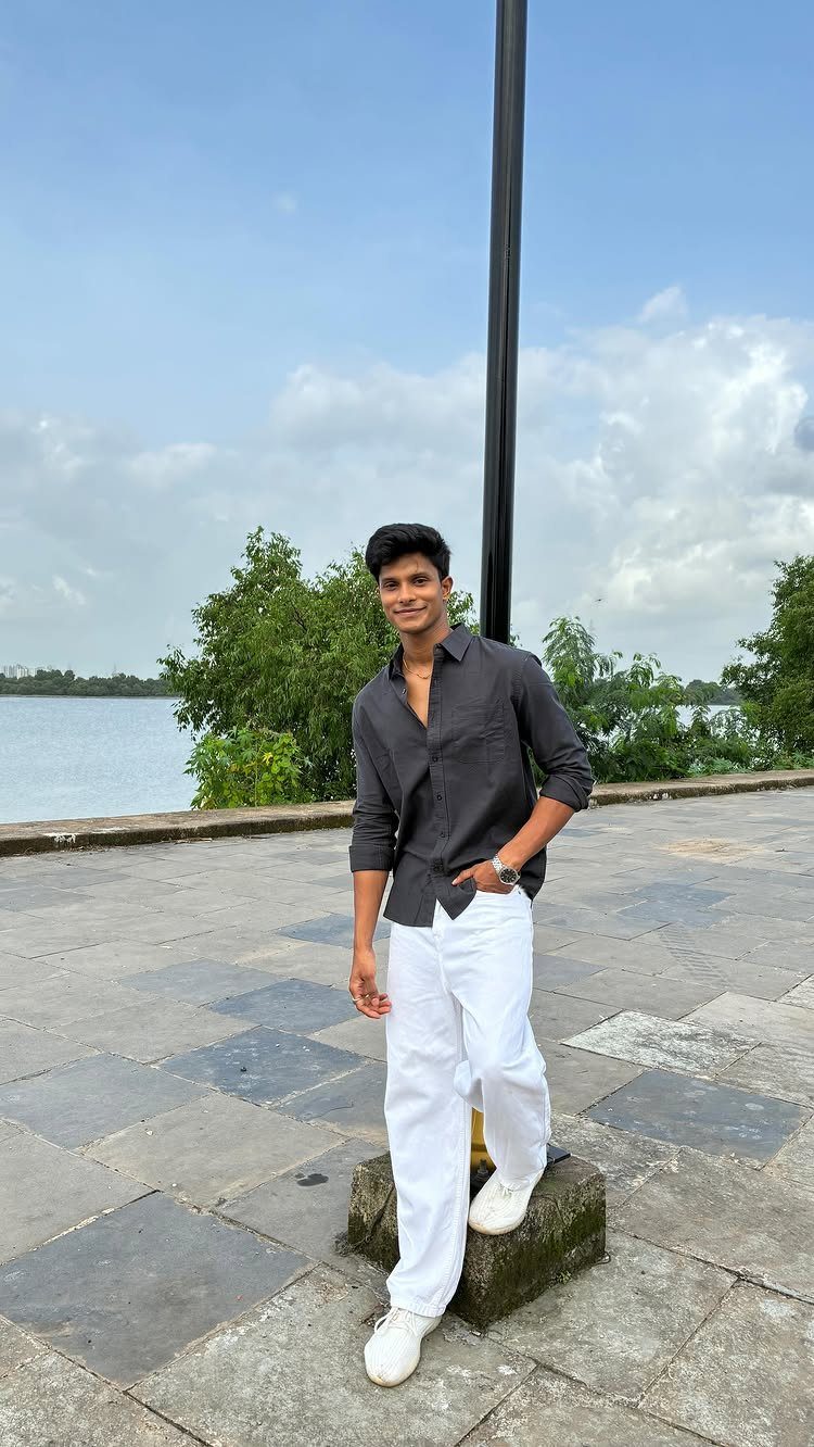 Young man in grey shirt and white trousers posing by a lake.