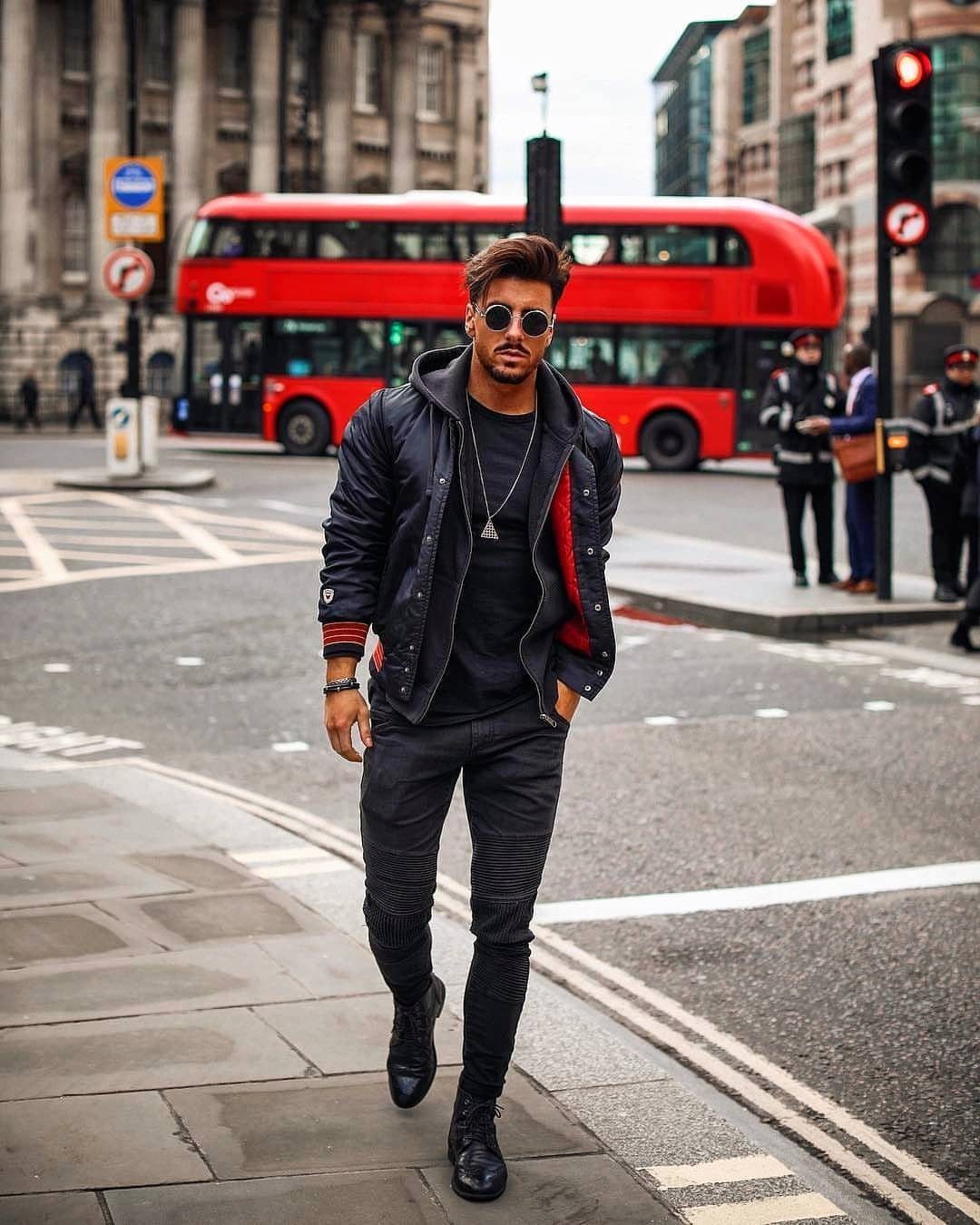 Man in all-black urban outfit posing on a London street with red bus.