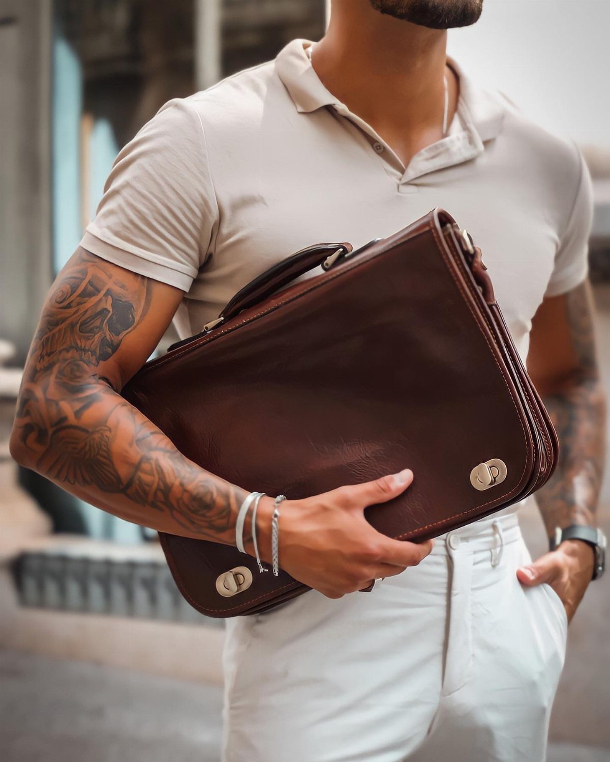Man in beige polo holding a dark brown leather briefcase under his arm.