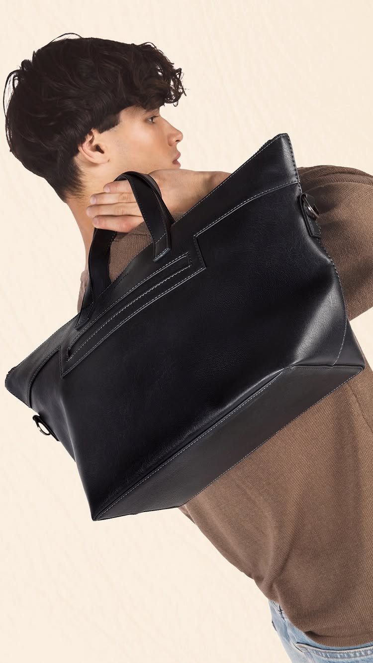 Man in brown sweater holding a large, structured black leather tote bag.