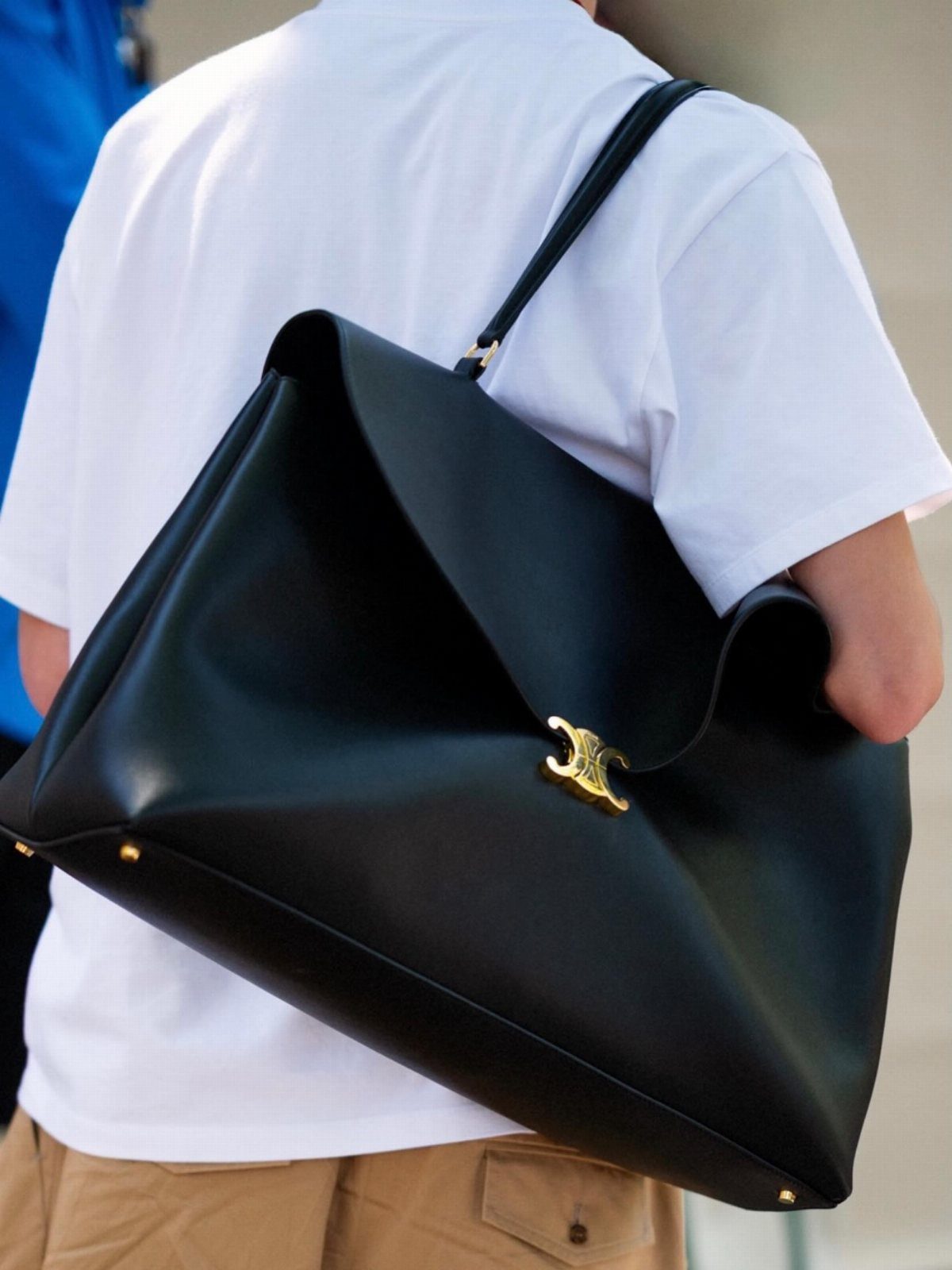Large black leather fashion purse with gold clasp carried by a man.
