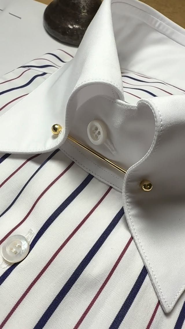 White striped dress shirt with a gold collar pin securing the pointed collar.