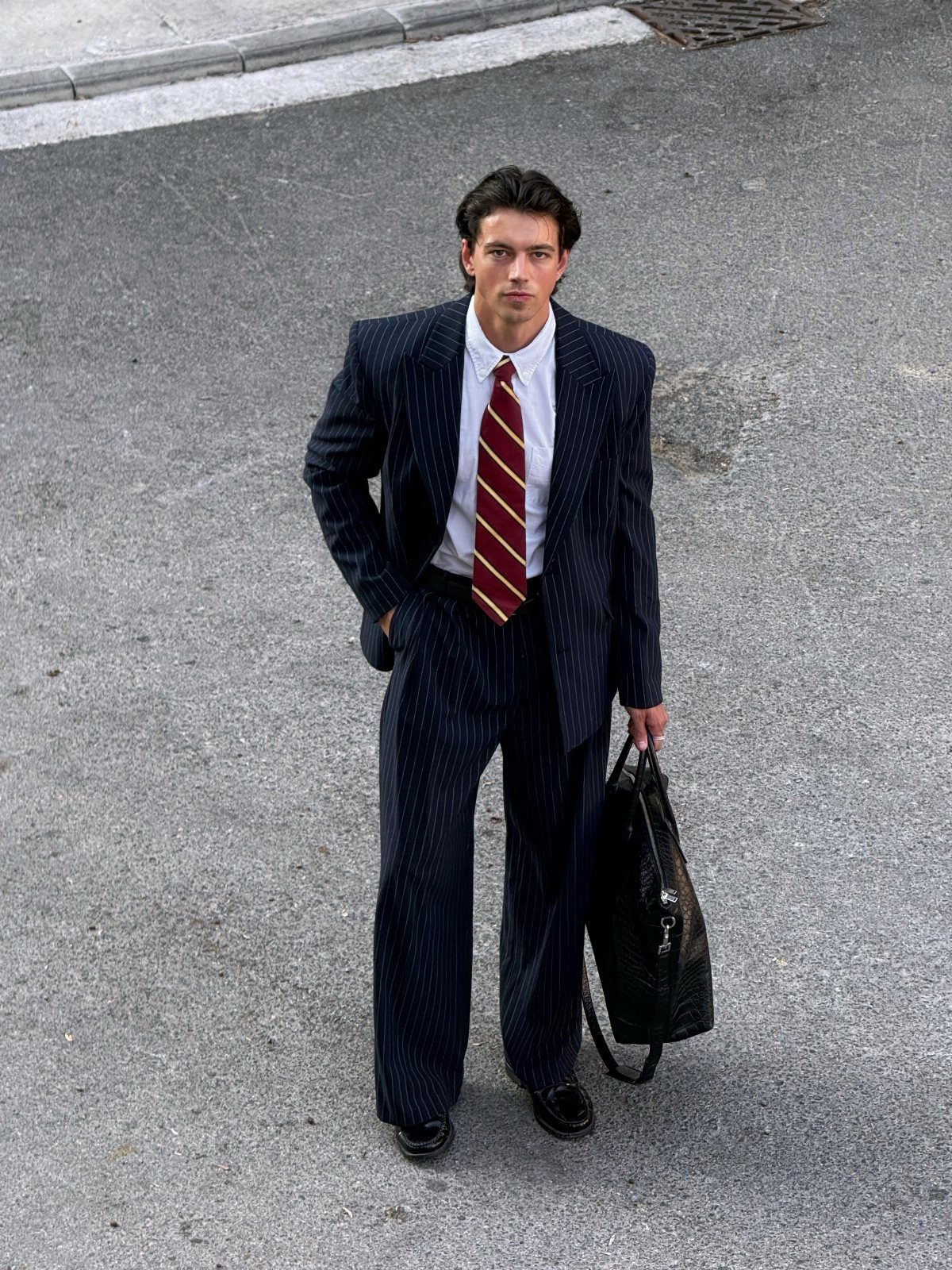 Slender man in navy pinstripe suit and striped tie holding a black briefcase.
