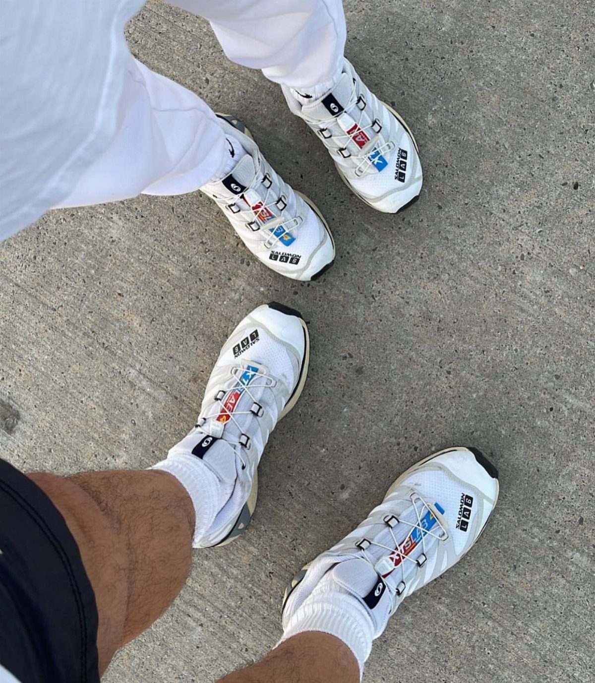 White technical gorpcore sneakers with quick-lace systems on a grey concrete ground.