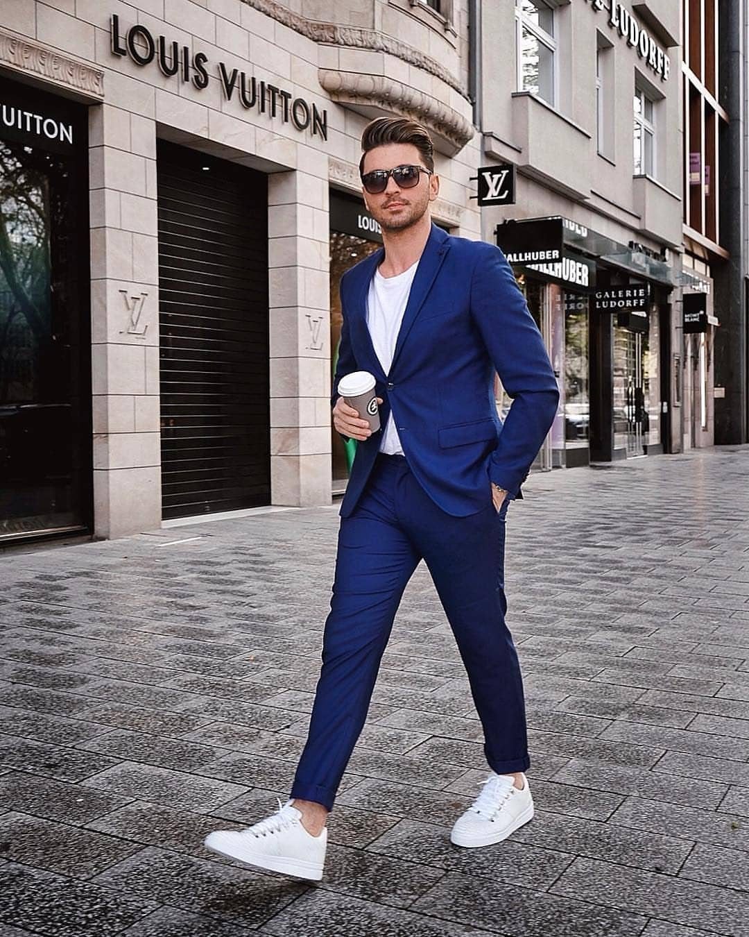 Man in a blue suit and white sneakers walking past a luxury store.