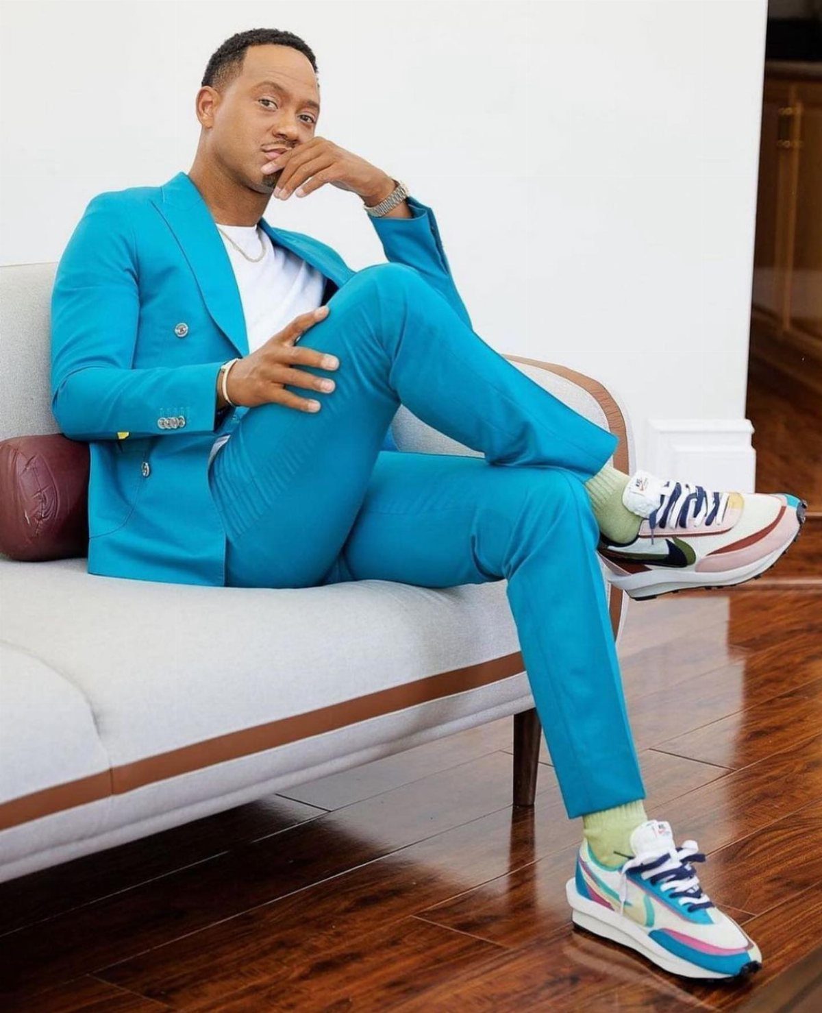 Man in a blue suit sitting on a sofa wearing colorful fashion sneakers.