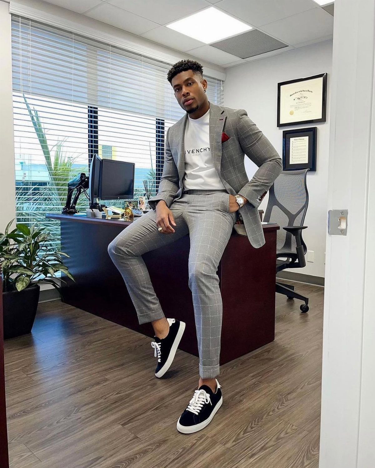 Man in a grey plaid suit wearing black low-top sneakers in an office.