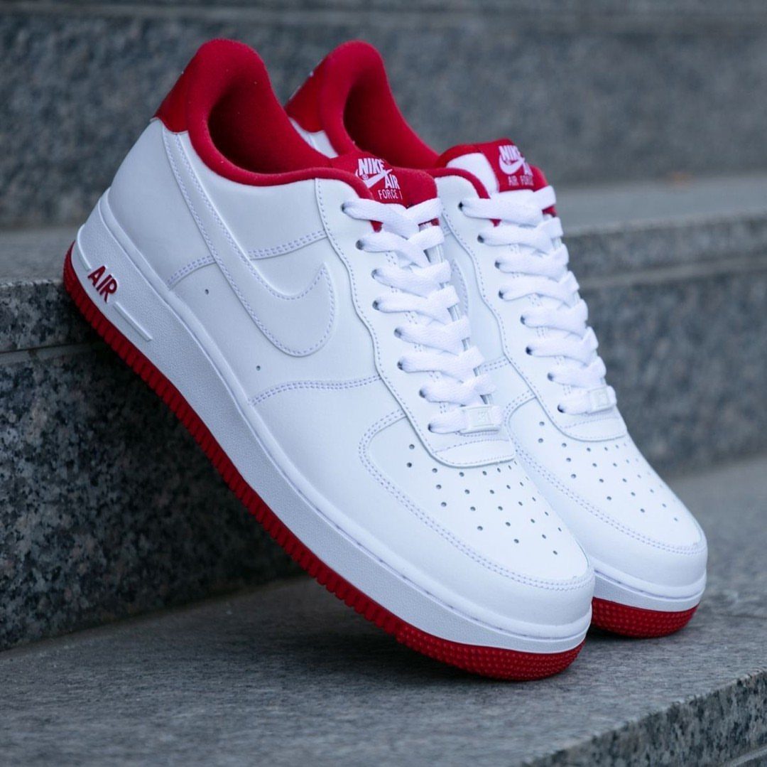 White Nike Air Force 1 sneakers with red soles on grey stone steps.