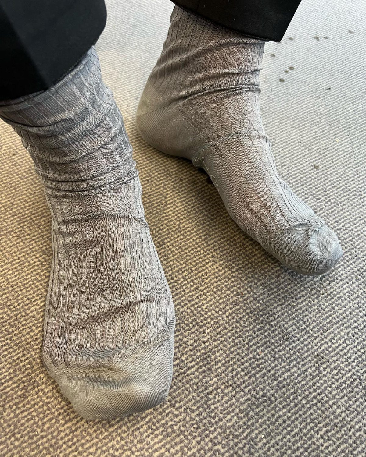 Grey ribbed crew socks worn with black trousers on a grey carpet.