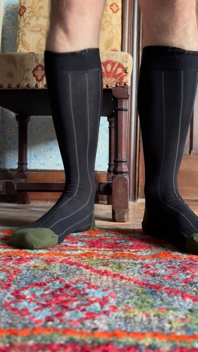 Black knee-high fashion socks with vertical stripes and green toes on a colorful rug.
