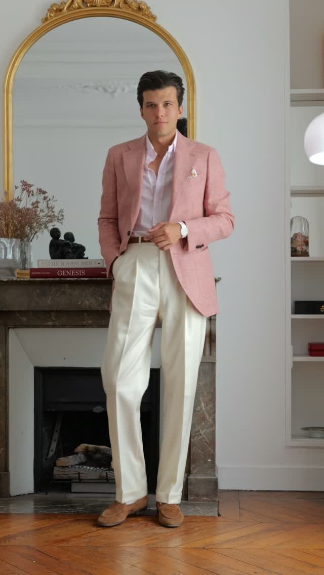 Man wearing a pink blazer, cream trousers, and brown suede derbies in a room.